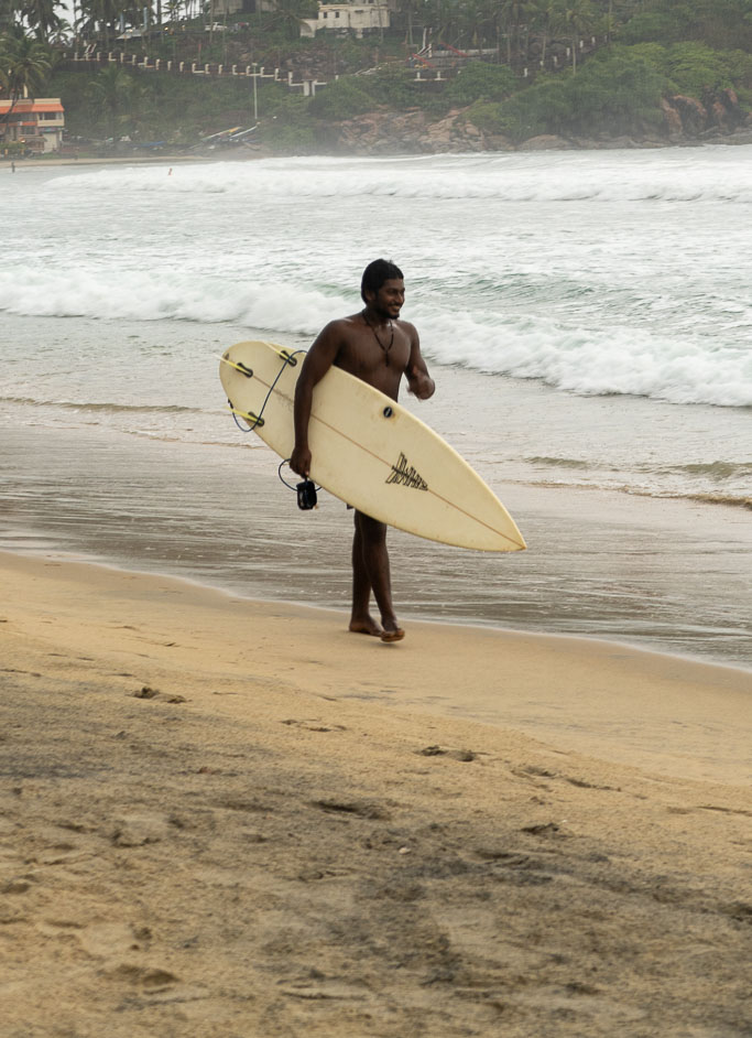 Boy walking with surfing board in kovalam beach- trivandrum,kerala